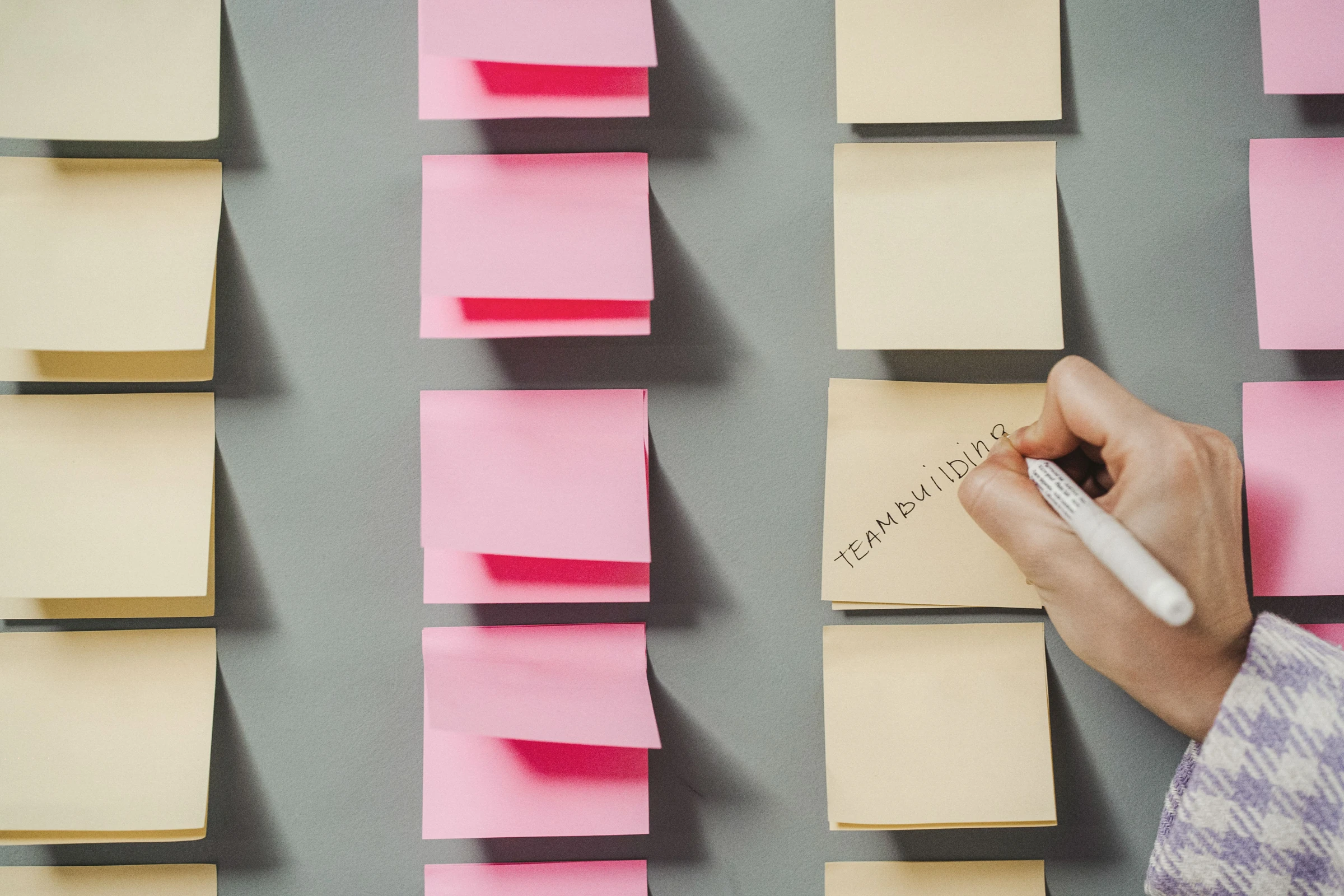 A hand writes a team-building note among pastel sticky notes.